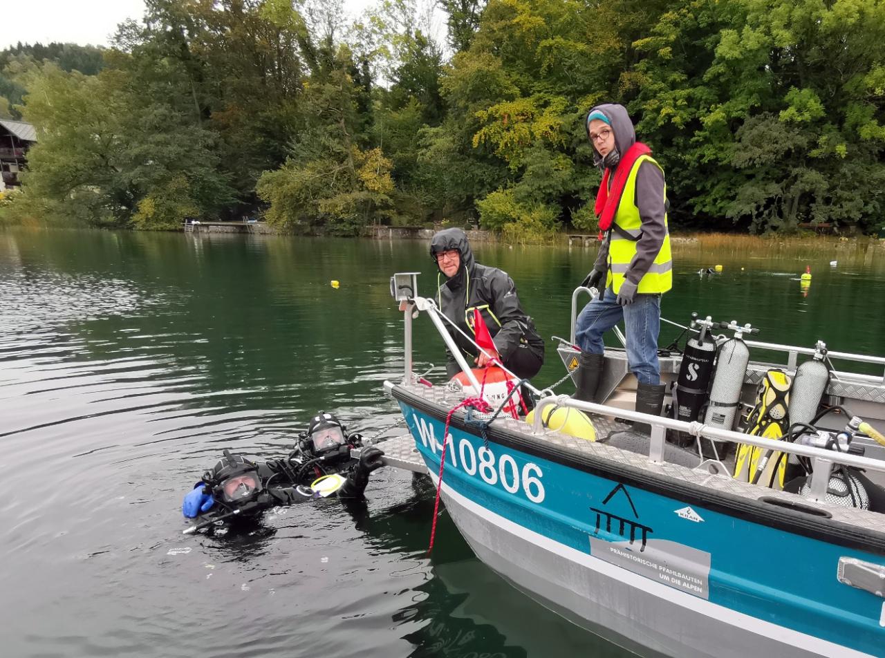 Ein Boot, auf dem sich 2 Personen befinden. Im Wasser davor sieht man 2 Taucher
