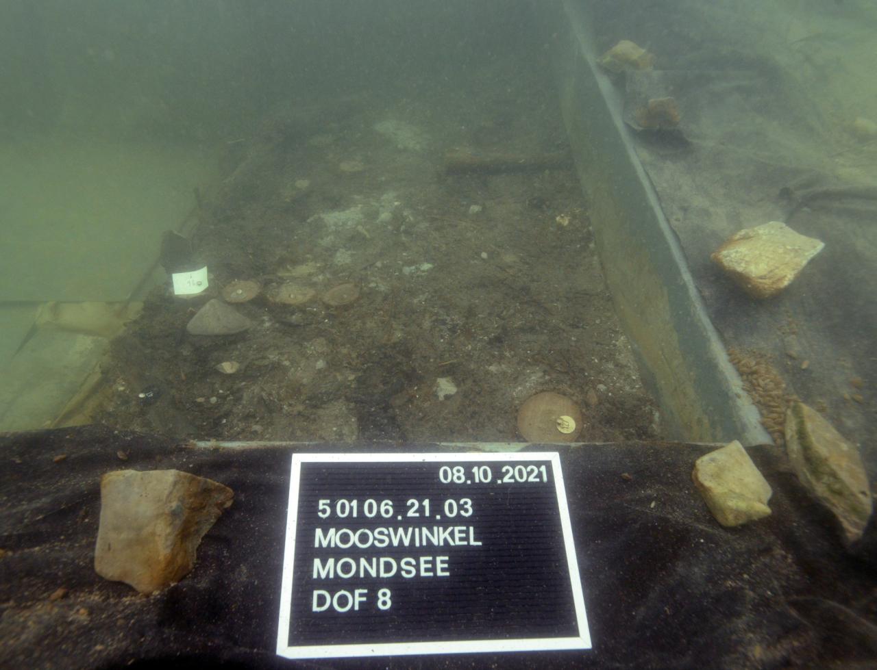 Eine Grabungsfläche unter Wasser mit einer Fototafel