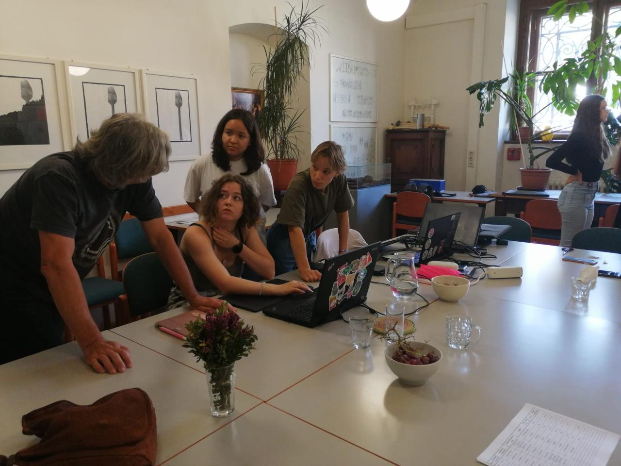 4 Personen stehen um einen Laptop gebeugt vor einem Tisch