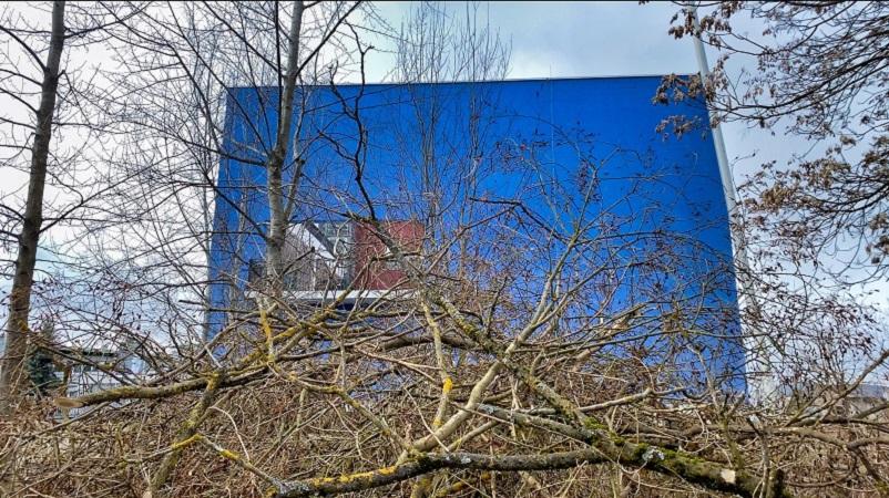 Ein blaues Haus, davor liegt ein großer Haufen Äste