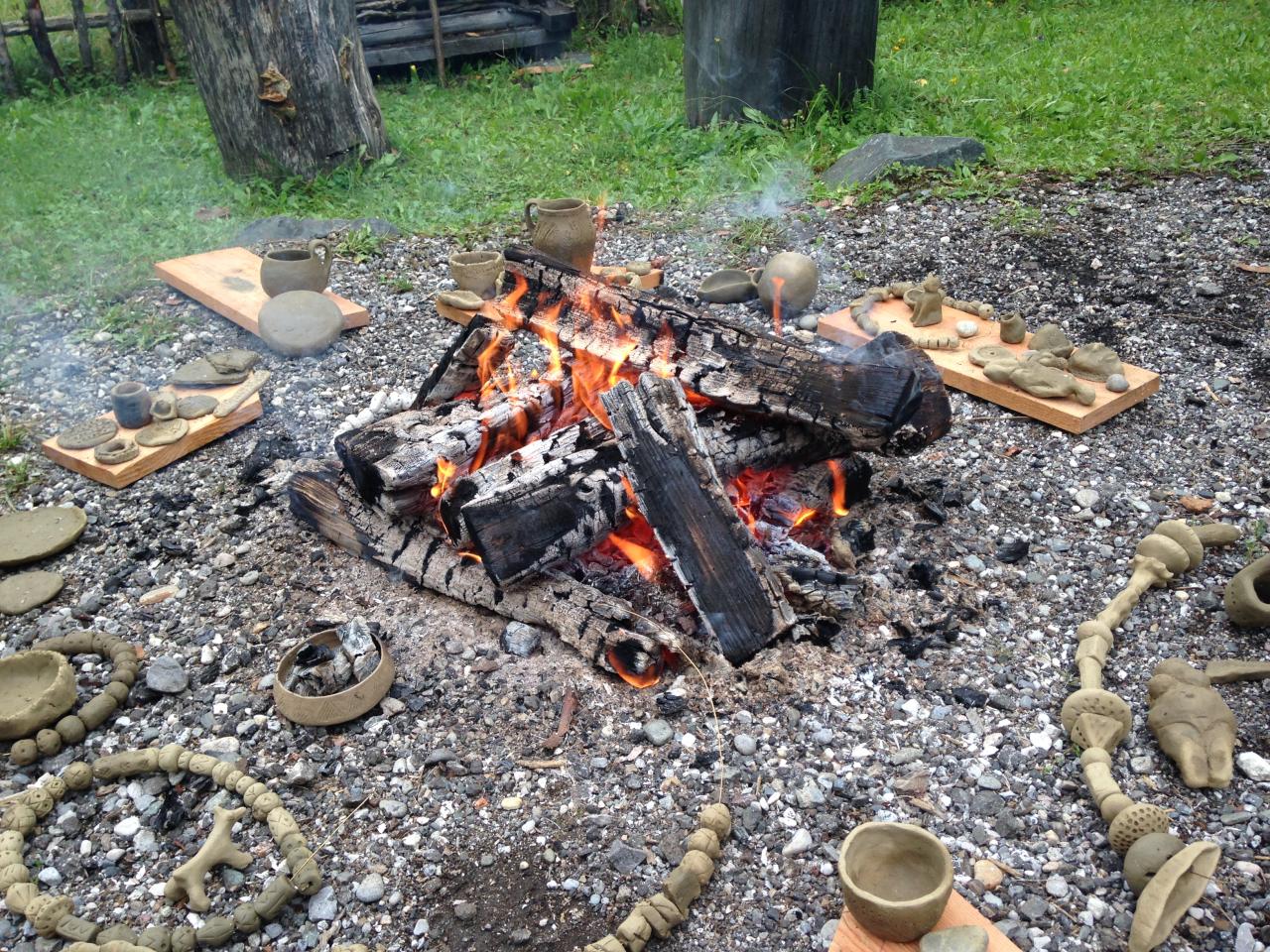 Feuchte Keramikgefäße liegen rund um brennende Holzscheite
