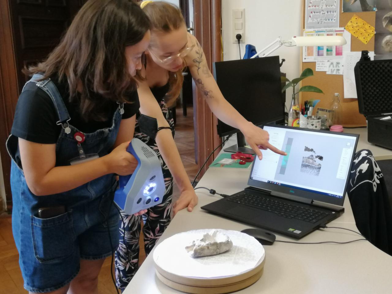 2 Personen, die mit einem Handscanner einen Gusslöffel scannen und das Ergebnis am Laptop betrachten.