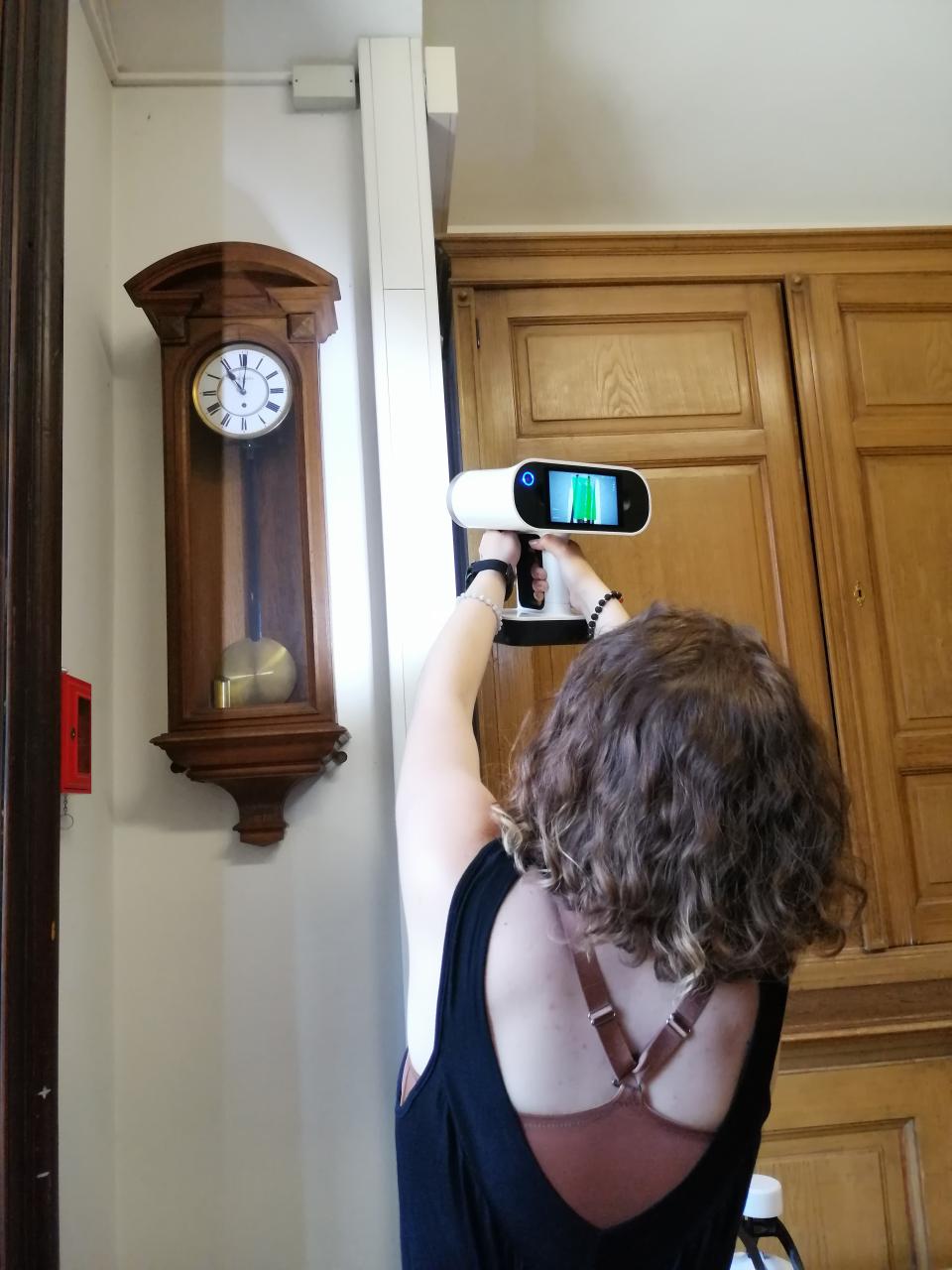 Eine Person, die eine Wandpendeluhr mit dem tragbaren 3D Scanner scannt.