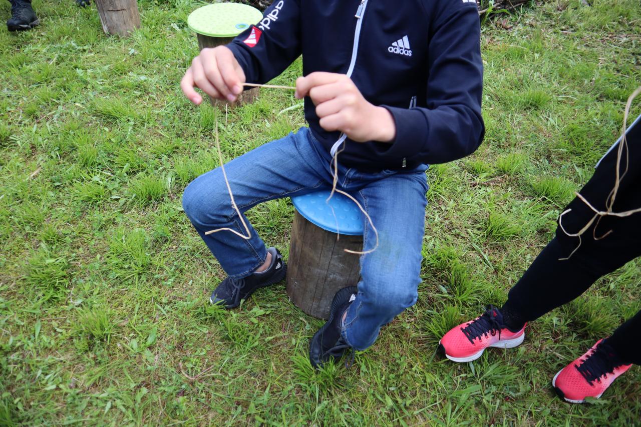 Eine Person sitzt auf einem Hocker und dreht eine Bastschnur