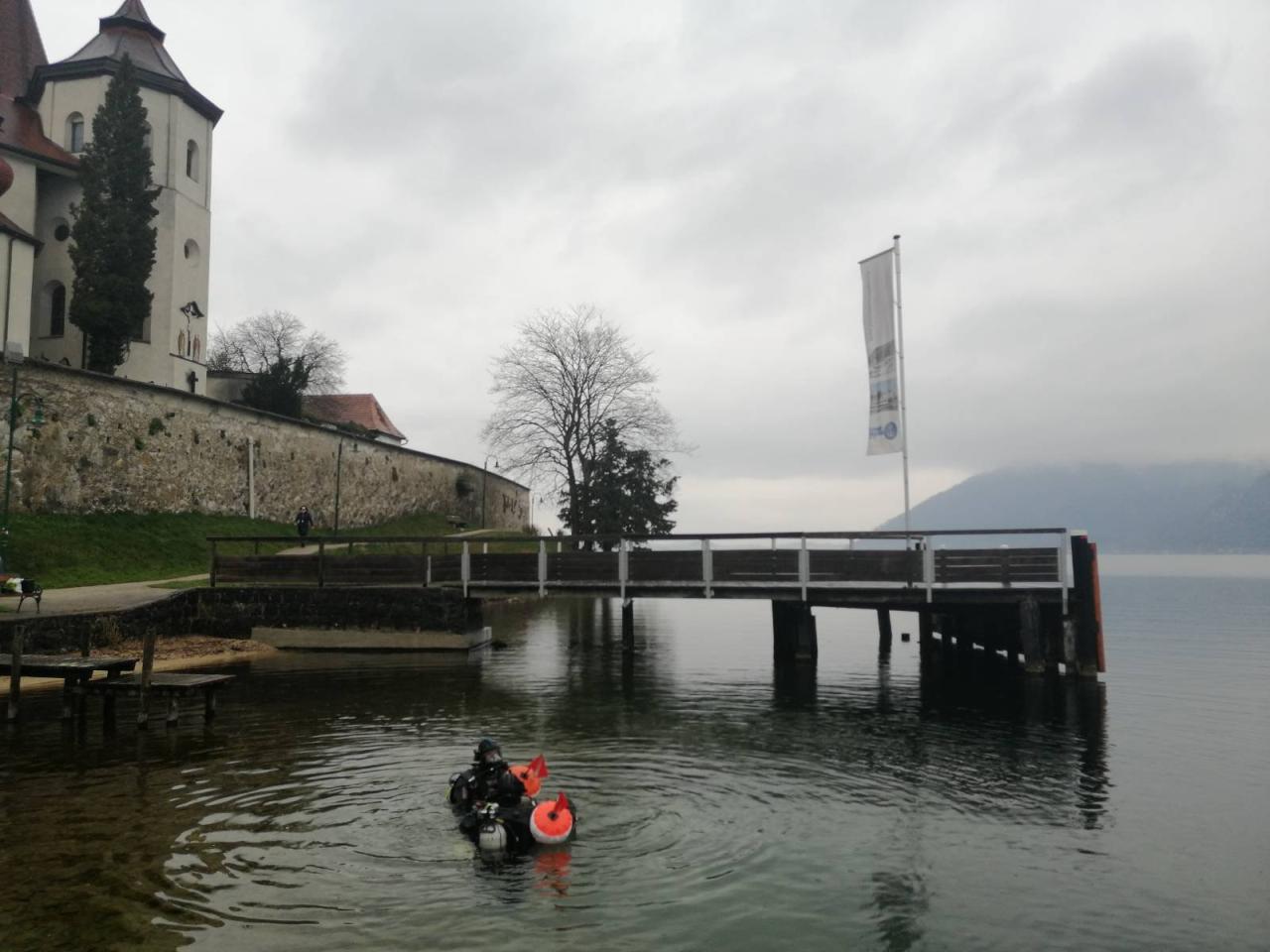 Taucher:Innen im Flachwasserbereich des Traunsees vor dem Hintergrund des Klosters Traunkirchen