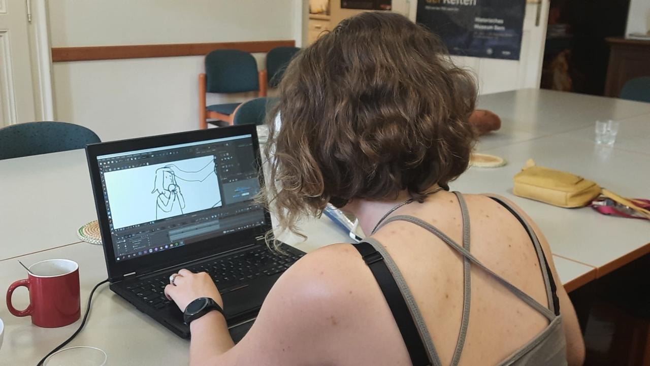 Eine Person sitzt vor einem Laptop an einem Tisch