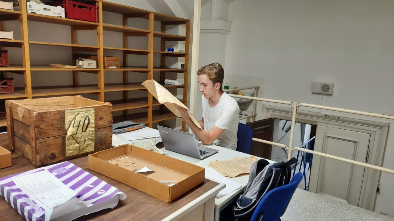 Eine Person sitzt in einem Archiv und liest eine alte Zeitung