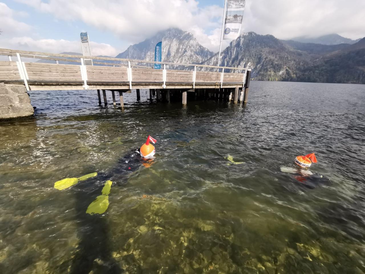 2 Taucher mit Bojen schwimmen im Seichtbereich vor einem Steg
