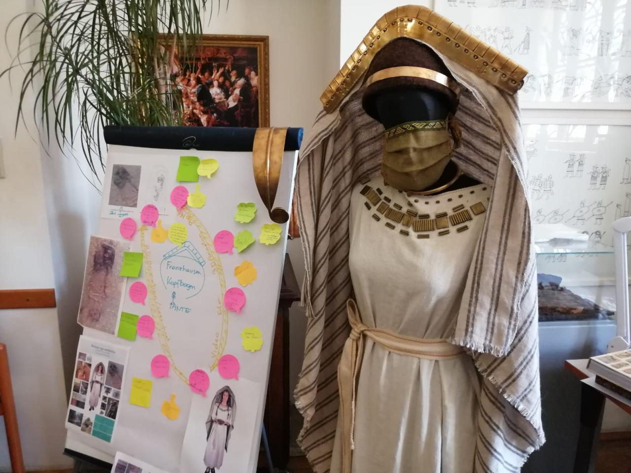 Eine Kleiderpuppe mit einem Gewand, dass nach dem bronzezeitlichen Fund in Franzhausen rekonstruiert wurde. Daneben ein Flipchart mit bunten Aufklebern