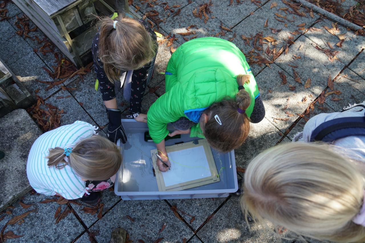 4 Kinder, die sich über eine Schreibtafel beugen
