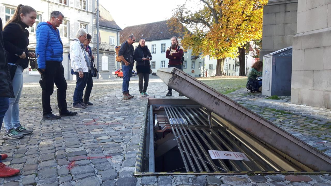 Mehrere Personen scharen sich um einen geöffneten Schachtdeckel im Kopfsteinpflaster
