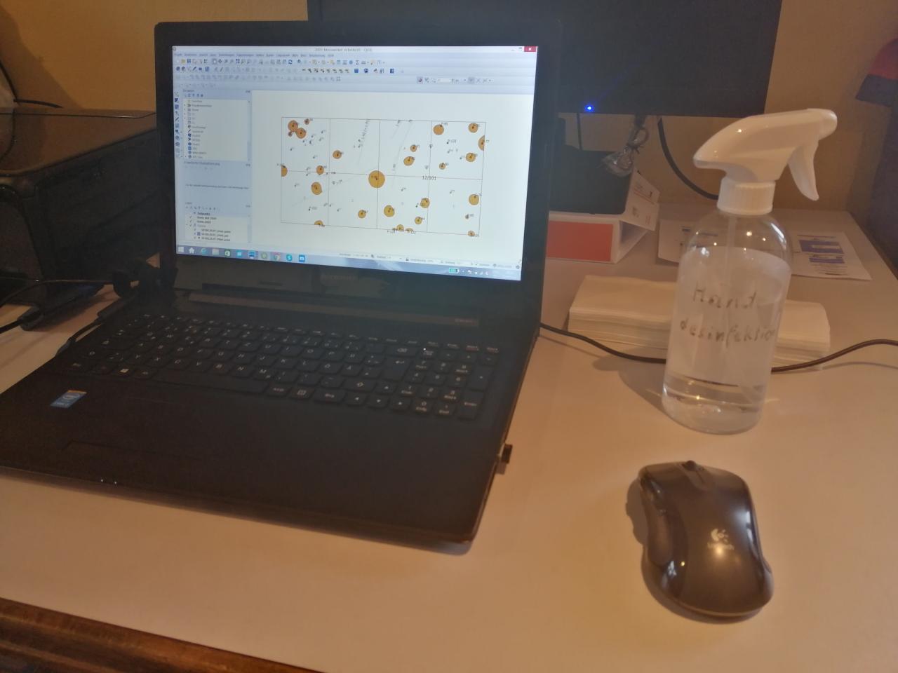 Ein geöffneter Laptop, daneben eine Computermaus und ein Desinfektionsspray