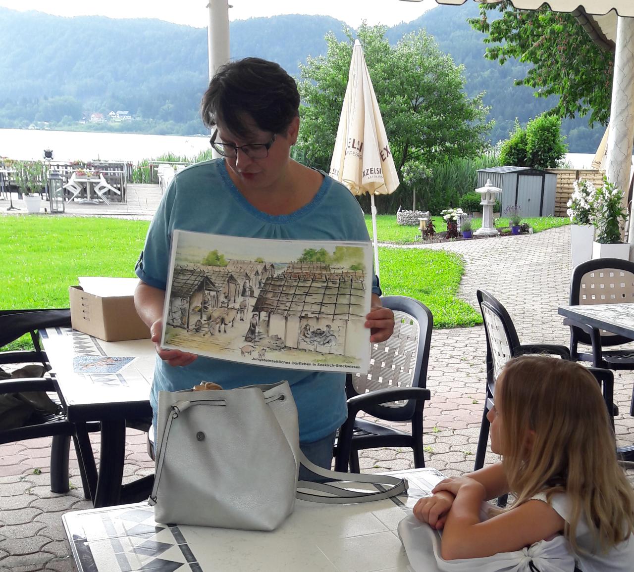 Lieselore erklärt Kindern etwas anhand einer Illustration in einem Strandcafe.