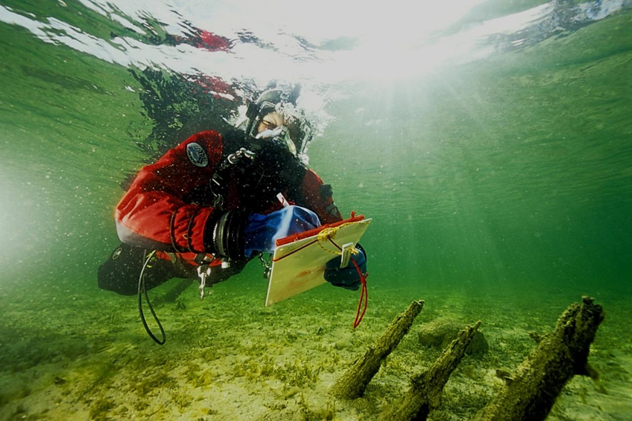 Ein Taucher unter Wasser, der Pfähle auf einer Schreibtafel dokumentiert