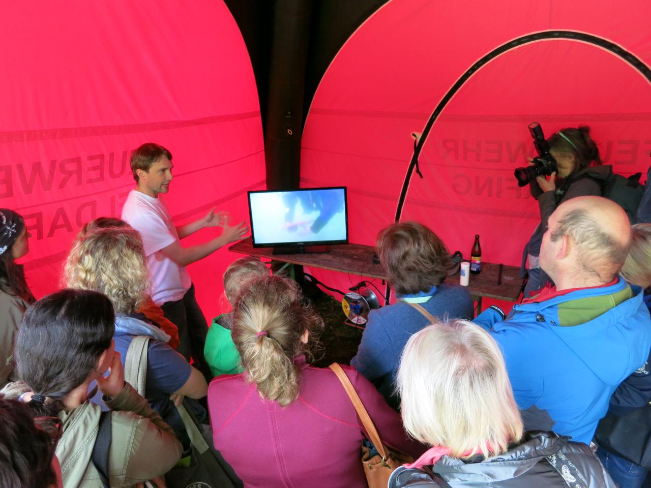 Eine Besuchergruppe sieht Live-Bilder auf einem Monitor von den Taucher:Innen unter Wasser