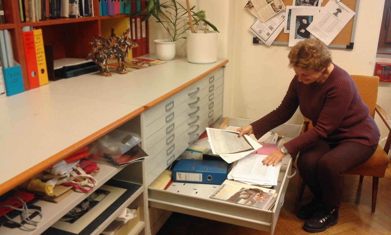 Eine Frau sitzt vor einer geöffneten Schublade mit Schriftstücken