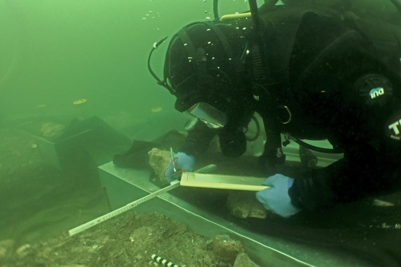Ein Taucher unter Wasser, der mit einem Maßstab und einer Schreibtafel hantiert
