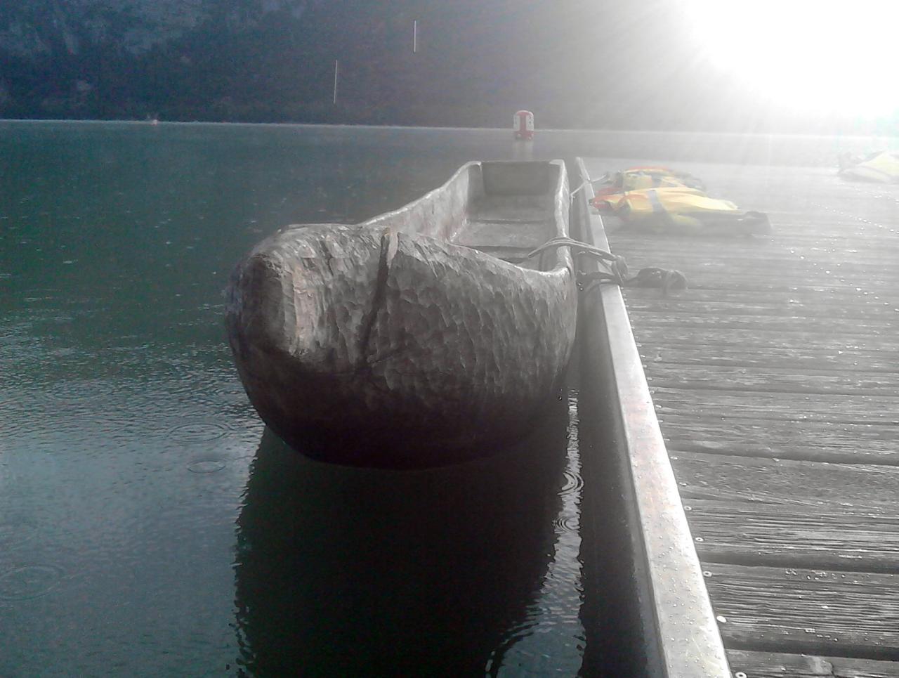 Ein Einbaum liegt angekettet an einem Steg im Wasser