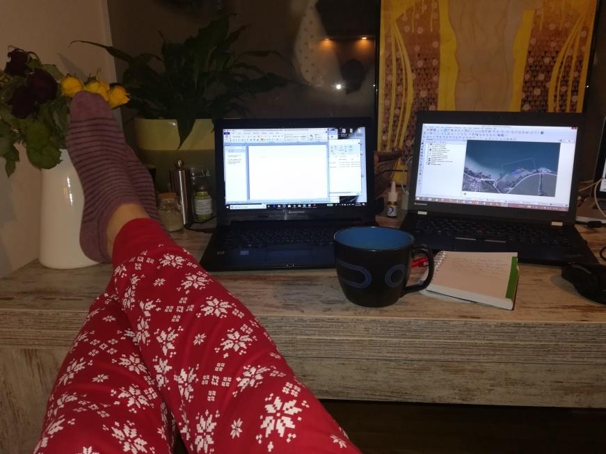 Man sieht Beine in einer roten Pyjama-Hose, die auf einem Schreibtisch liegen. Daneben eine Kaffeetasse und 2 Laptops