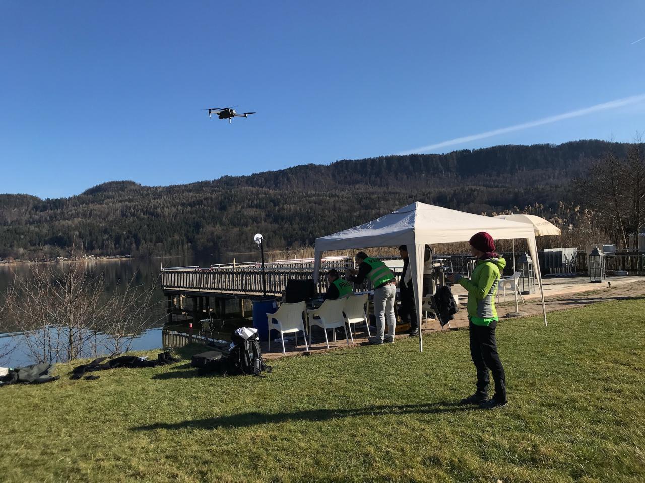 Eine Frau lenkt eine Drohne über den See, am Ufer ist ein weißer Pavillon aufgebaut
