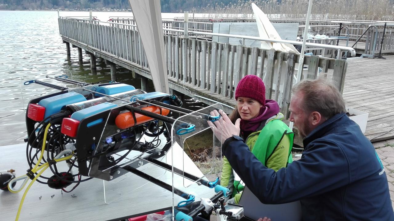 Vera und Cyril knien vor einem Tauchroboter "Manio", welcher auf einem Tisch steht