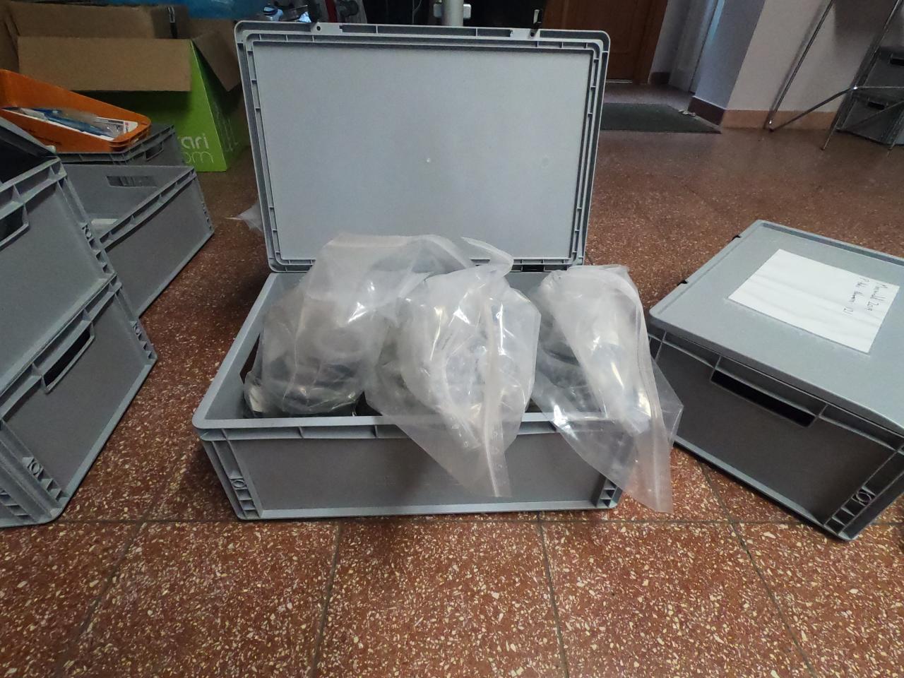 Eine vollgepackte, graue Plastikkiste steht zwischen weiteren ihrer Art