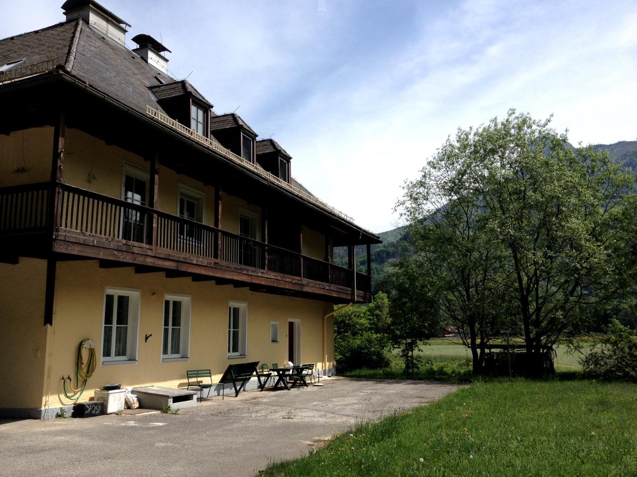 Ein dreigeschossiges, gelbes Gebäude mit rundumlaufendem Balkon inmitten einer Wiese