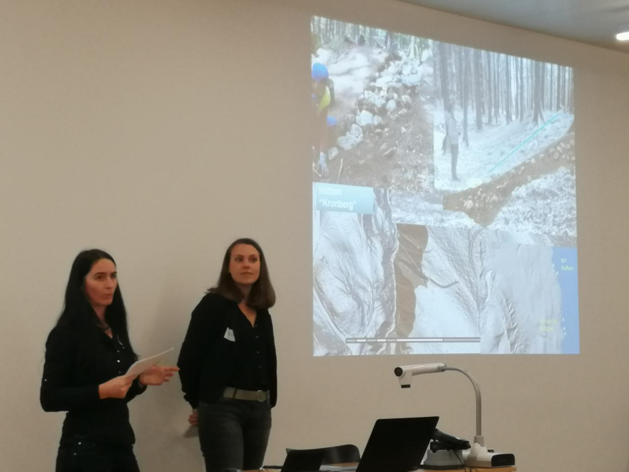 2 Frauen stehen vor einer Leinwand bei einem Vortrag