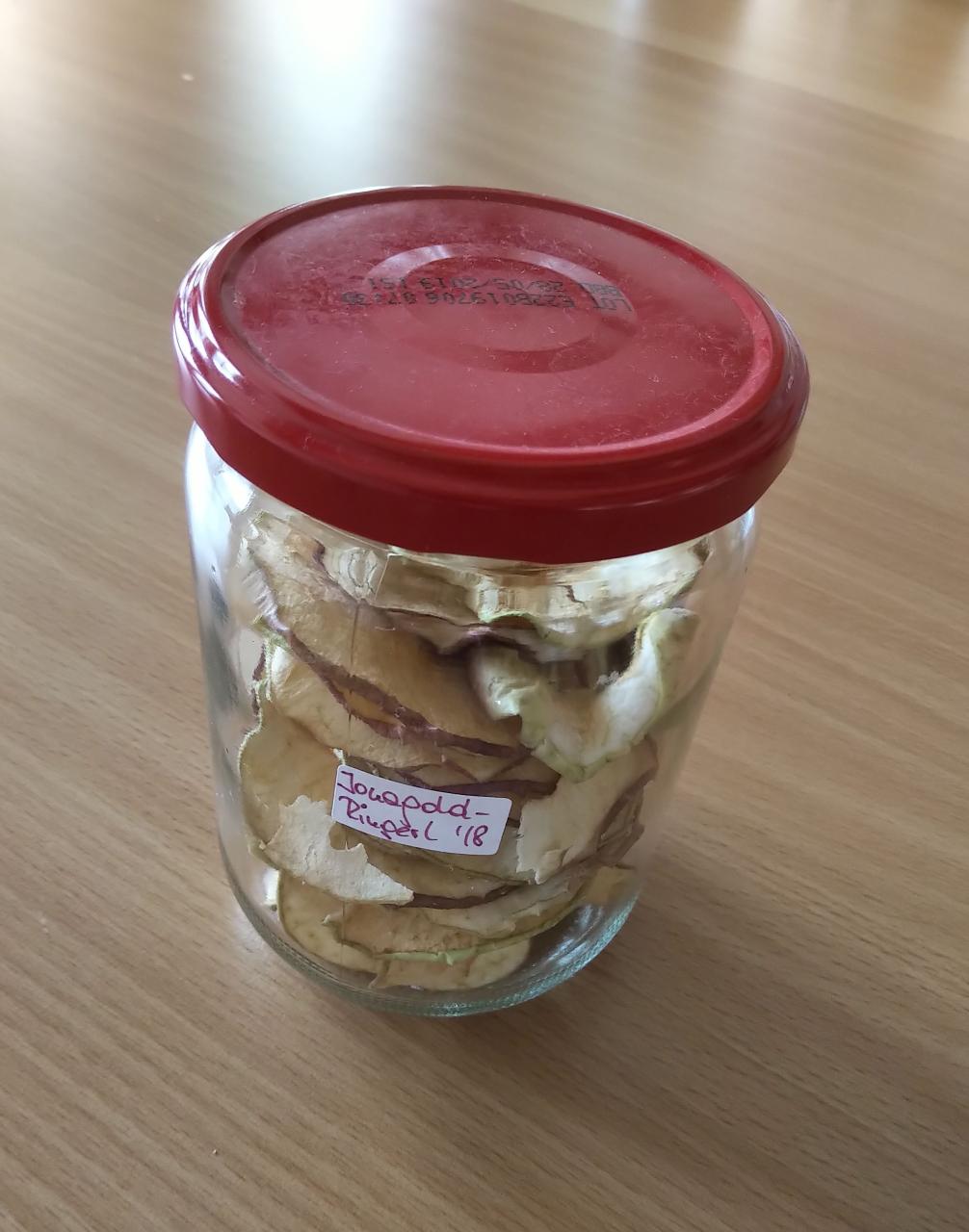 Ein Schraubglas mit rotem Deckel enthält getrocknete Apfelringe