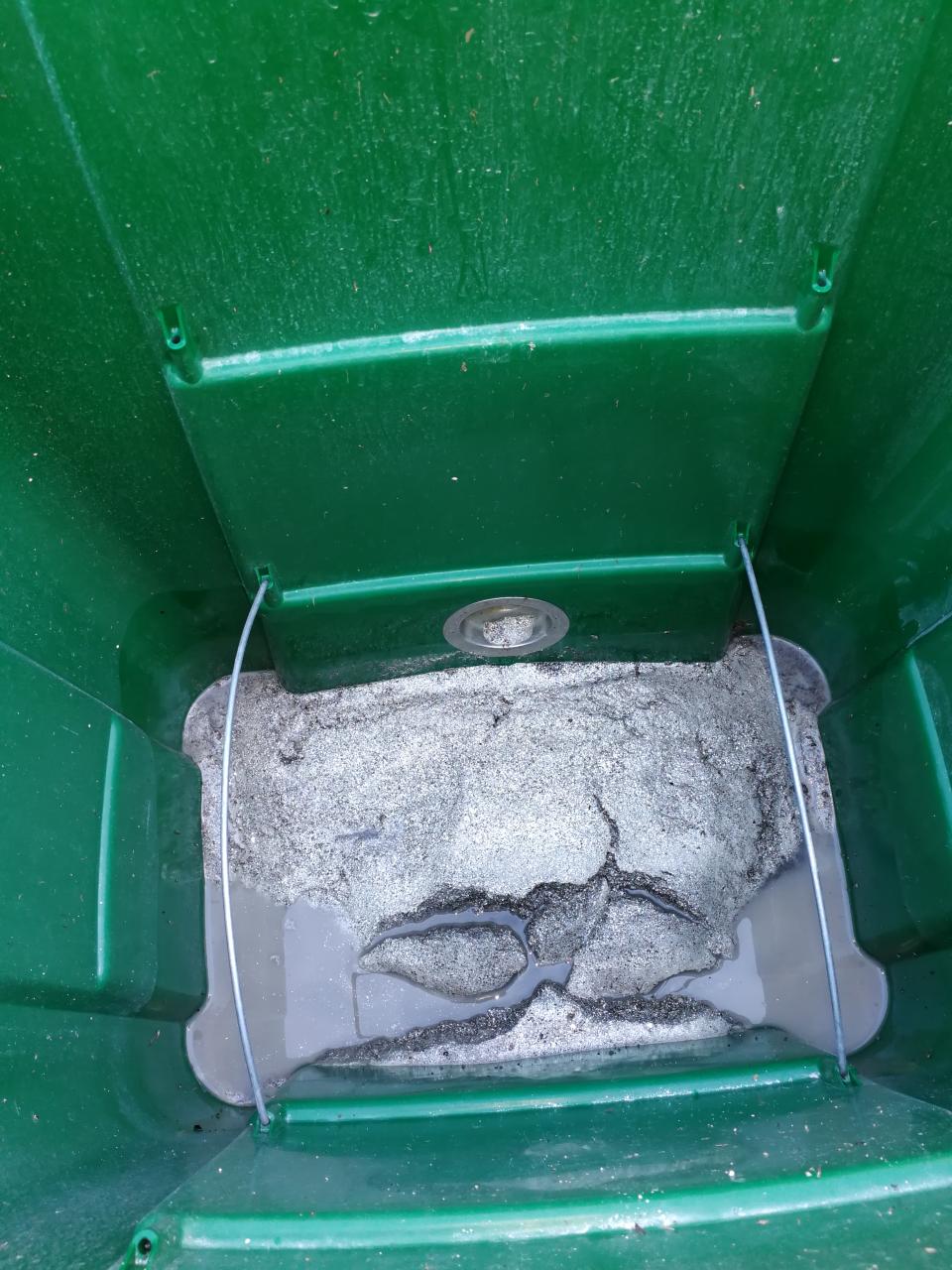 Eine grüne Plastiktonne, in der ein Bodensatz aus Schlämmresten liegt