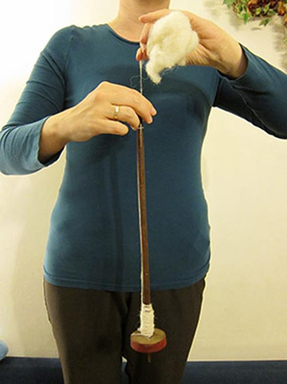 Eine Person hält eine Handspindel und Fasern vor sich 