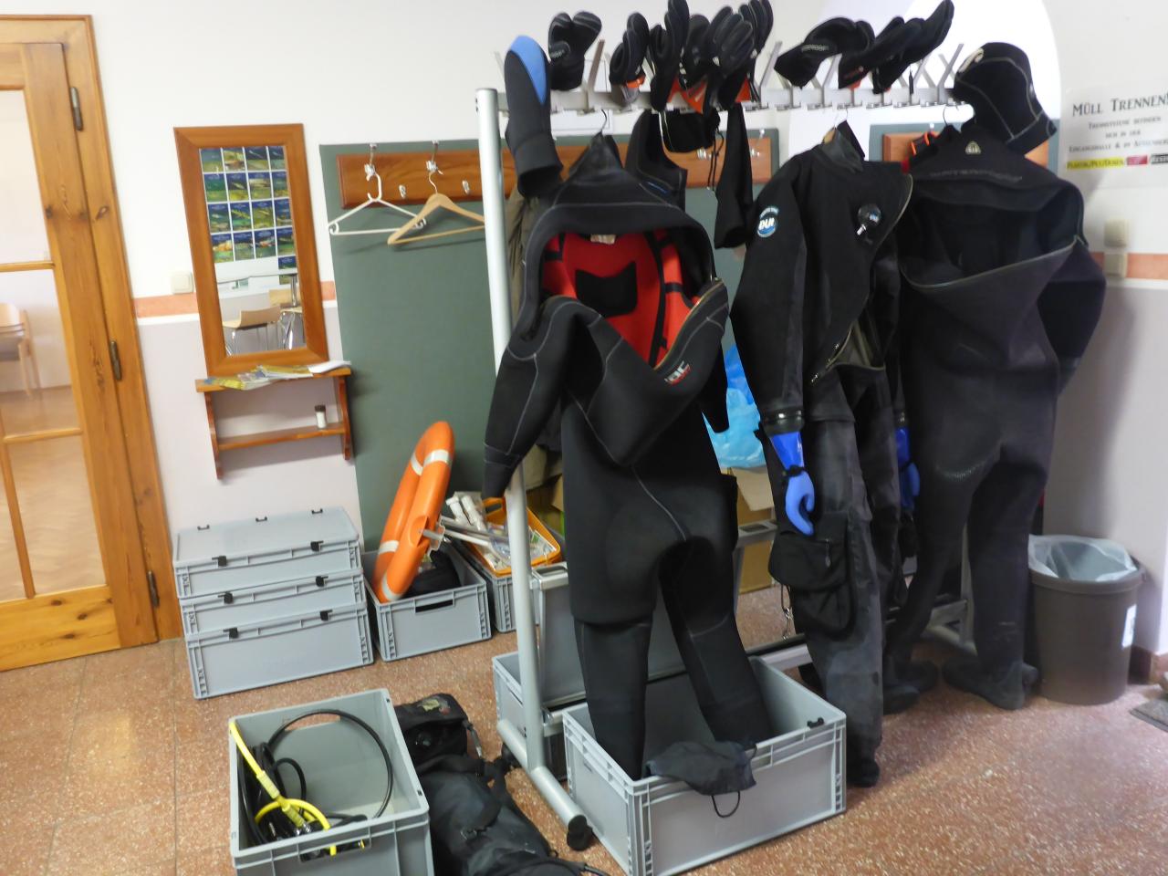 Trocken-Tauchanzüge hängen an Garderoben in einer Umkleide