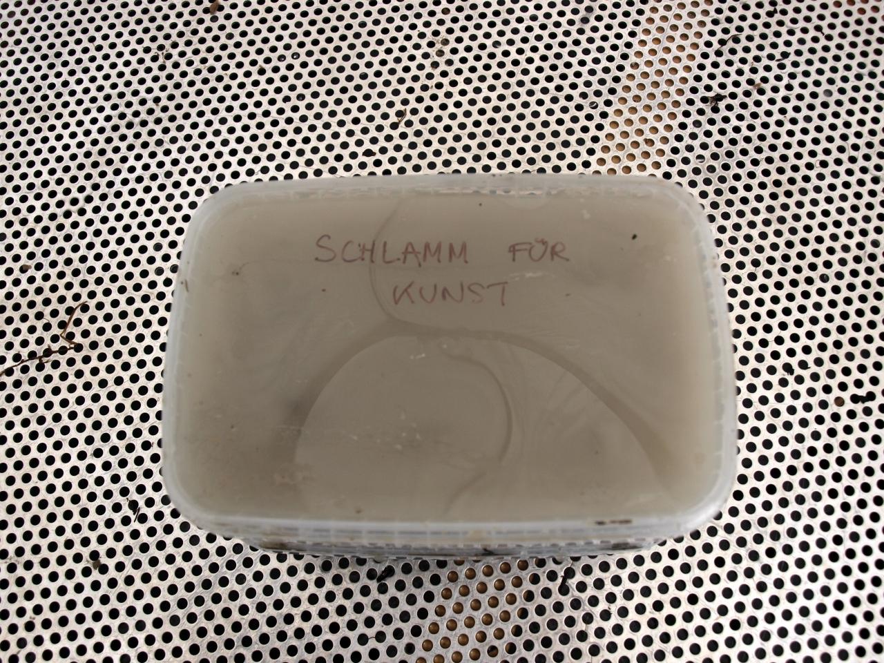 Ein Plastikbecher mit Schlamm und der Aufschrift "Schlamm für Kunst"