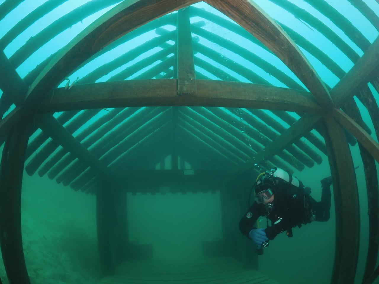 Eine Rekonstruktion eine Hauses unter Wasser, dazwischen ein Taucher