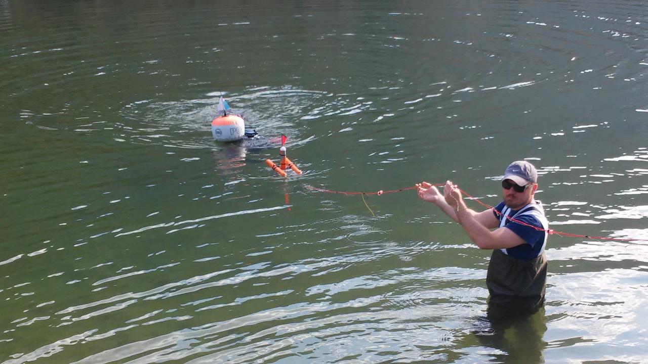 Eine Person steht halb im Wasser des Sees und zieht an einer Bojenleine