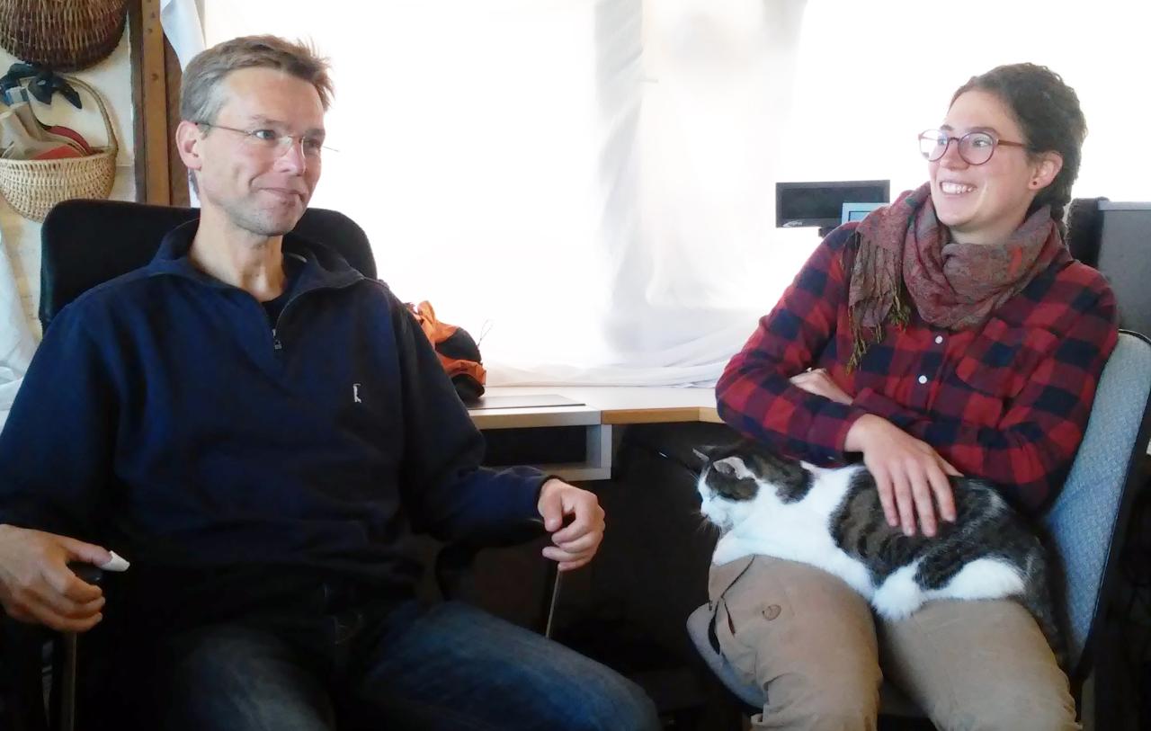 Henrik Pohl und Anna Jalkin (mit Katze auf dem Schoß) sitzen auf 2 Bürostühlen