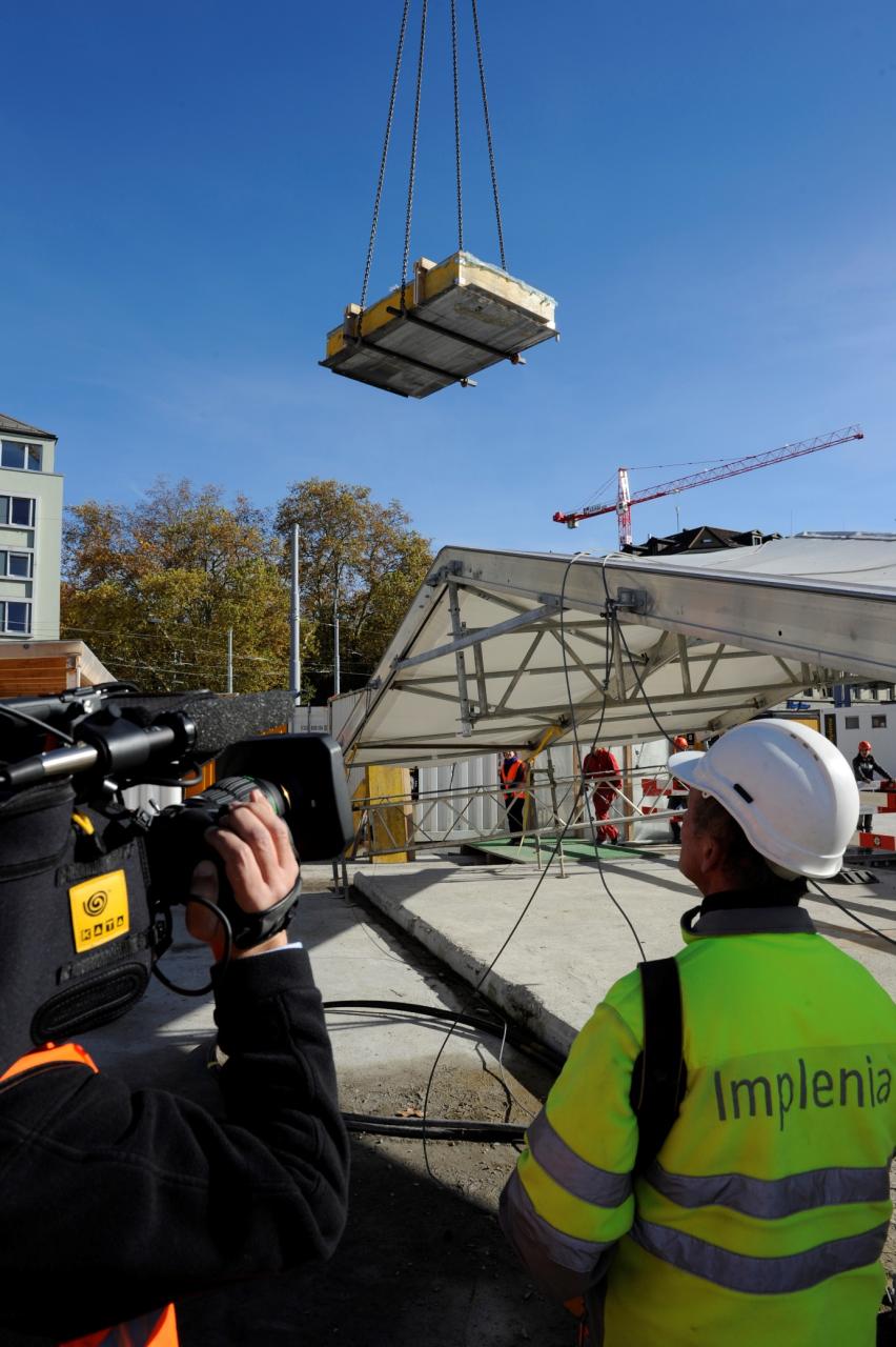 Ein Kran hievt die Türe über einen Platz und wird dabei gefilmt