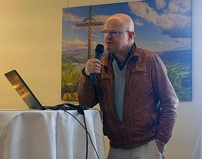 Timothy Taylor steht mit einem Mikrofon an einem Stehtisch, auf dem ein Laptop aufgebaut ist