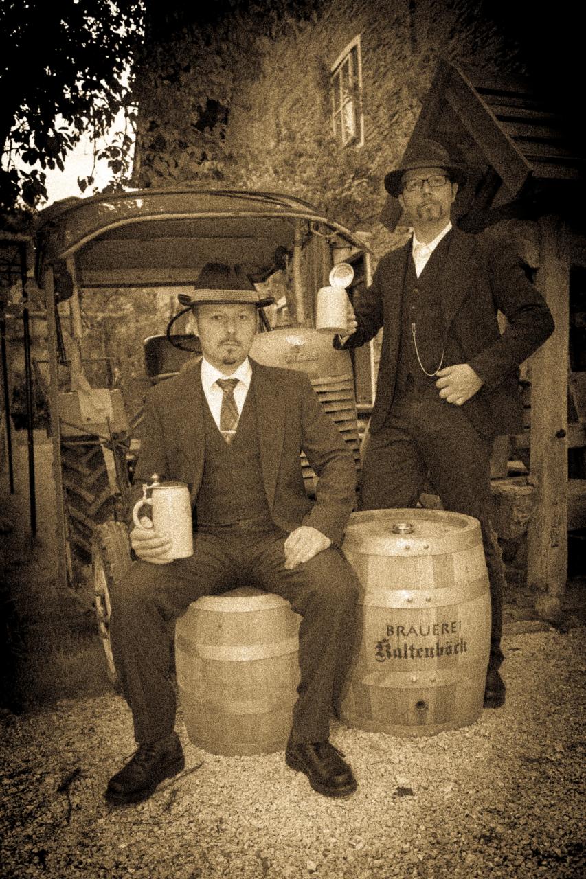 Die Brüder Kaltenböck neben Bierfässern und mit Bierkrügen in der Hand