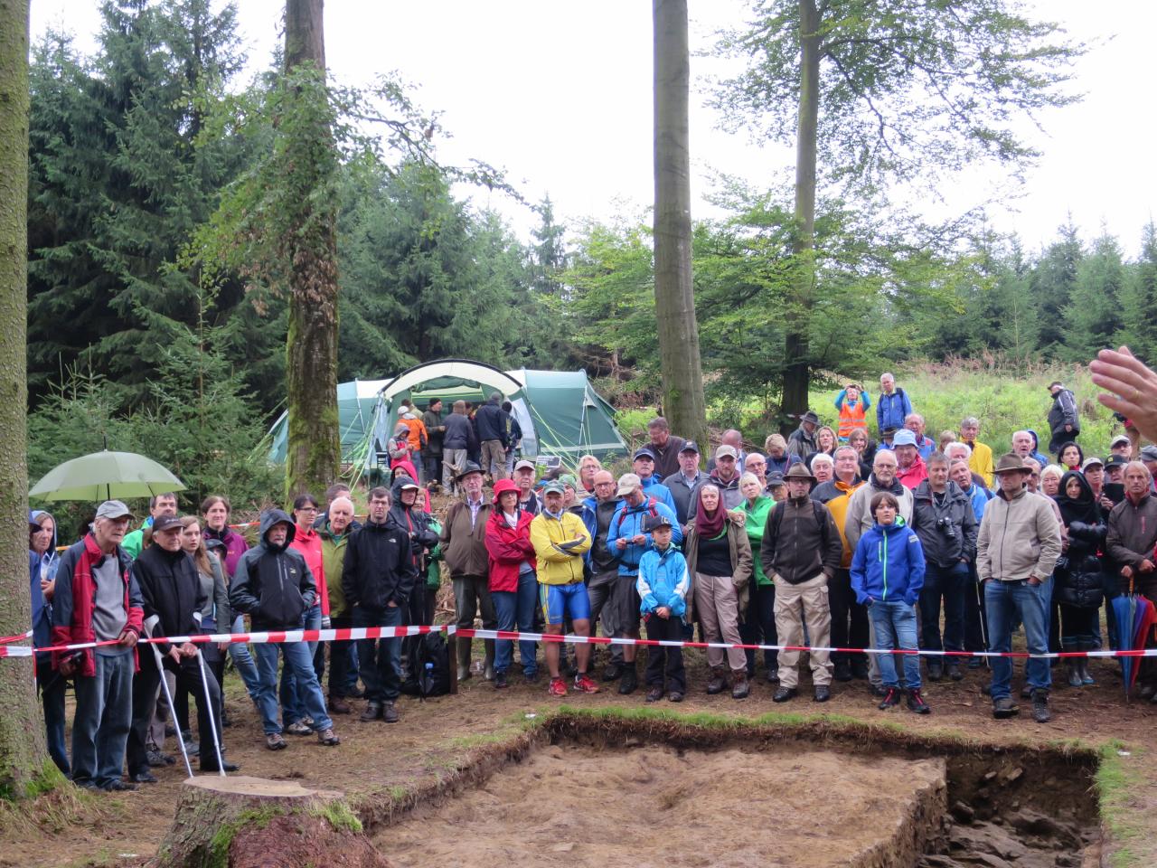 Eine große Besuchergruppe hinter Absperrband am Grabungsschnitt