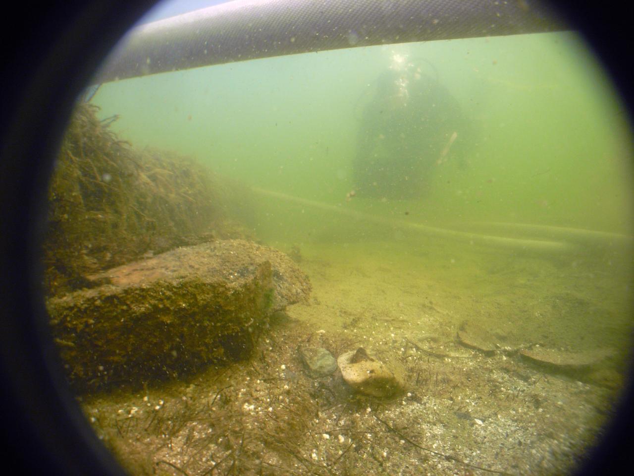 Man erkennt eine Randscherbe im trüben Wasser am Seegrund
