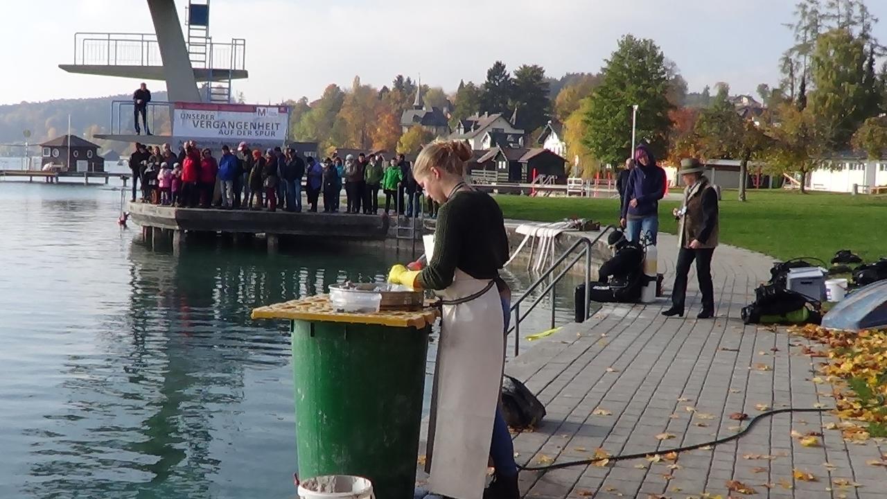 Im Vordergrund sieht man eine junge Frau an der Schlämmstation, dahinter macht sich Helena im Tauchanzug bereit ins Wasser zu steigen