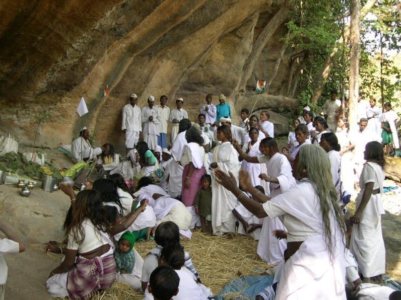 Eine große Menschengruppe, alle in weißen Gewändern, vor einer Felshöhle in Indien