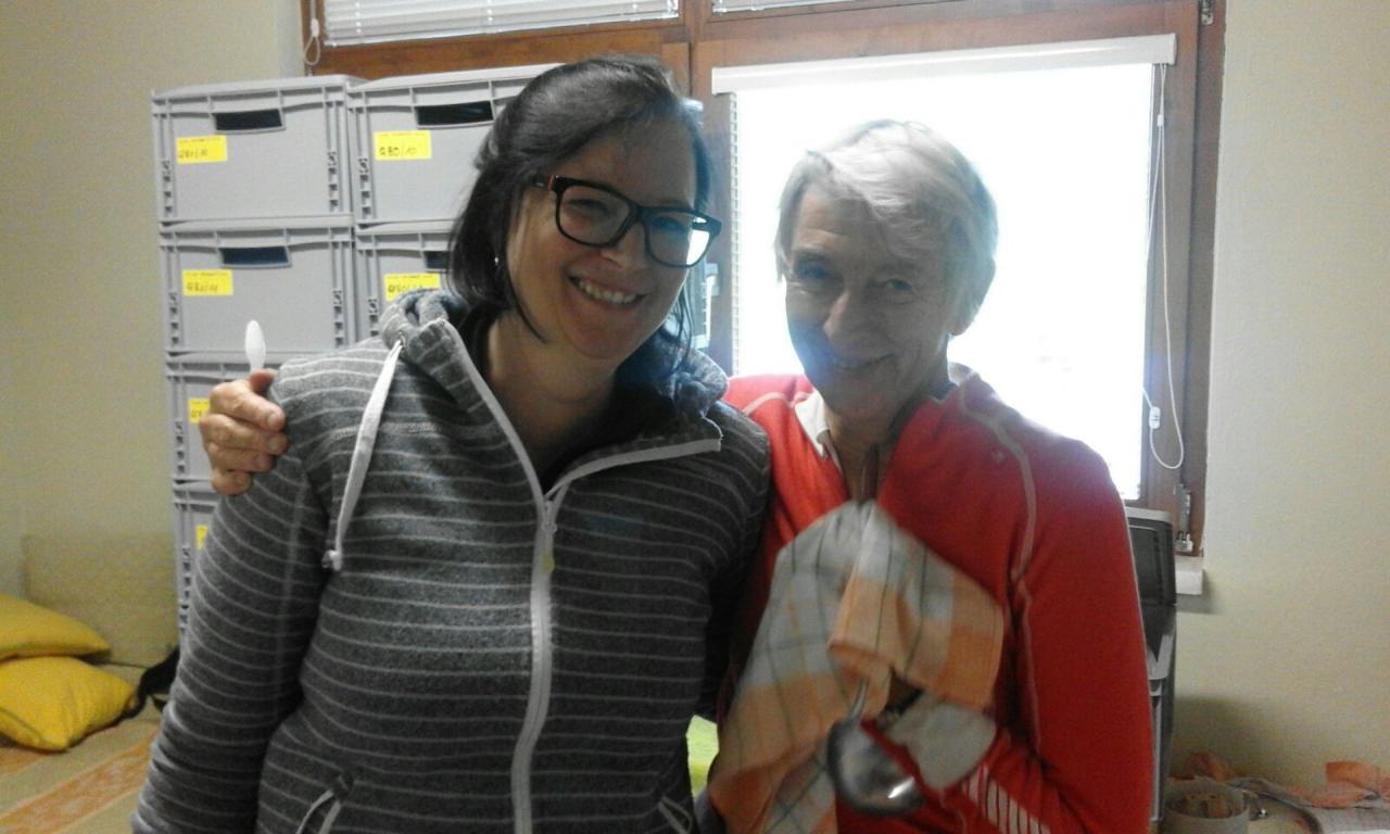 Bärbel und Heike umarmen sich vor einem Fenster und grauen Kisten