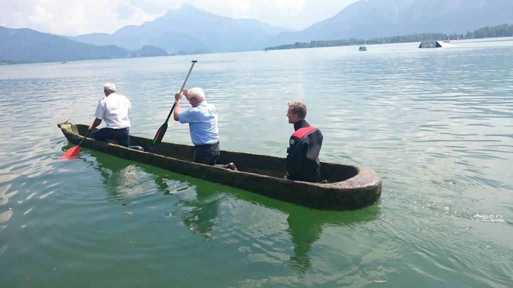 3 Männer an Bord des Einbaums paddeln über den See