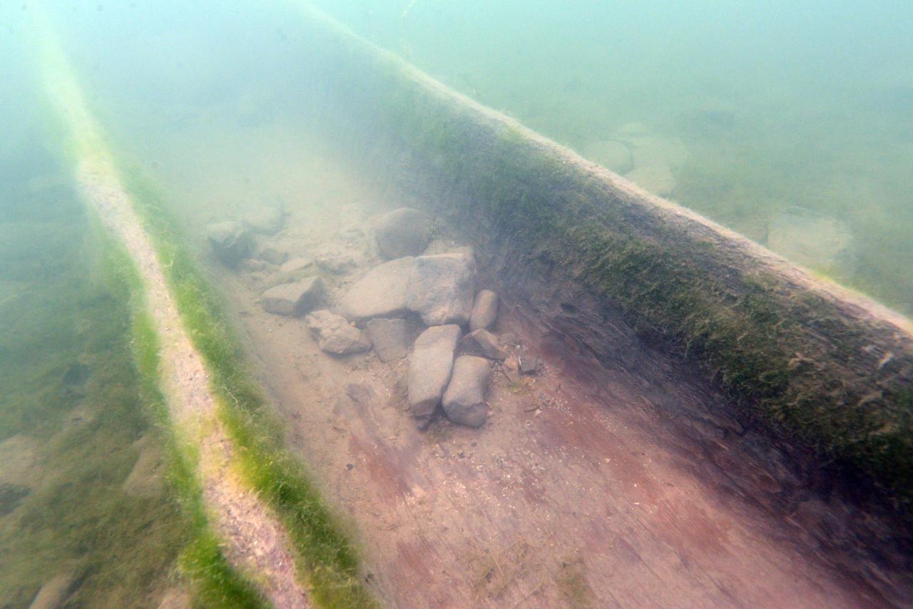 Der Mittelteil des Einbaums unter Wasser mit Steinen beschwert