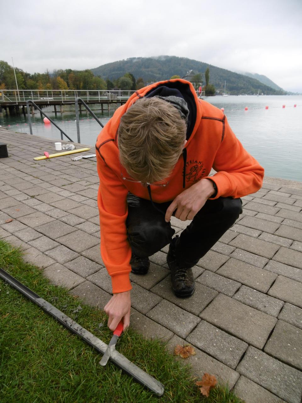 Ein Mann in oranger Jacke hockt gebeugt über einem, am Boden liegenden, Bohkern
