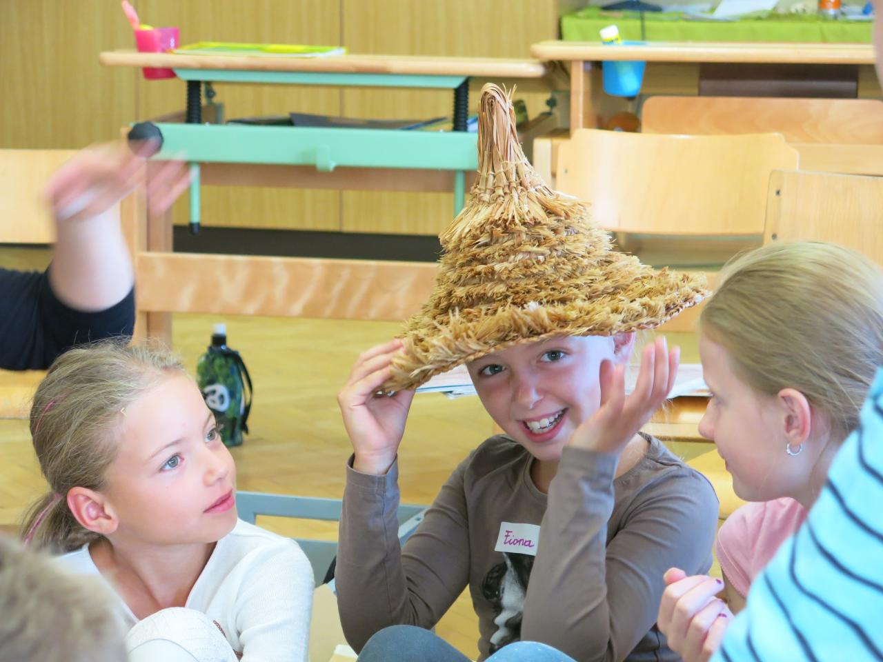 3 Kinder am Boden des Klassenzimmers, das mittlere trägt einen Strohhut