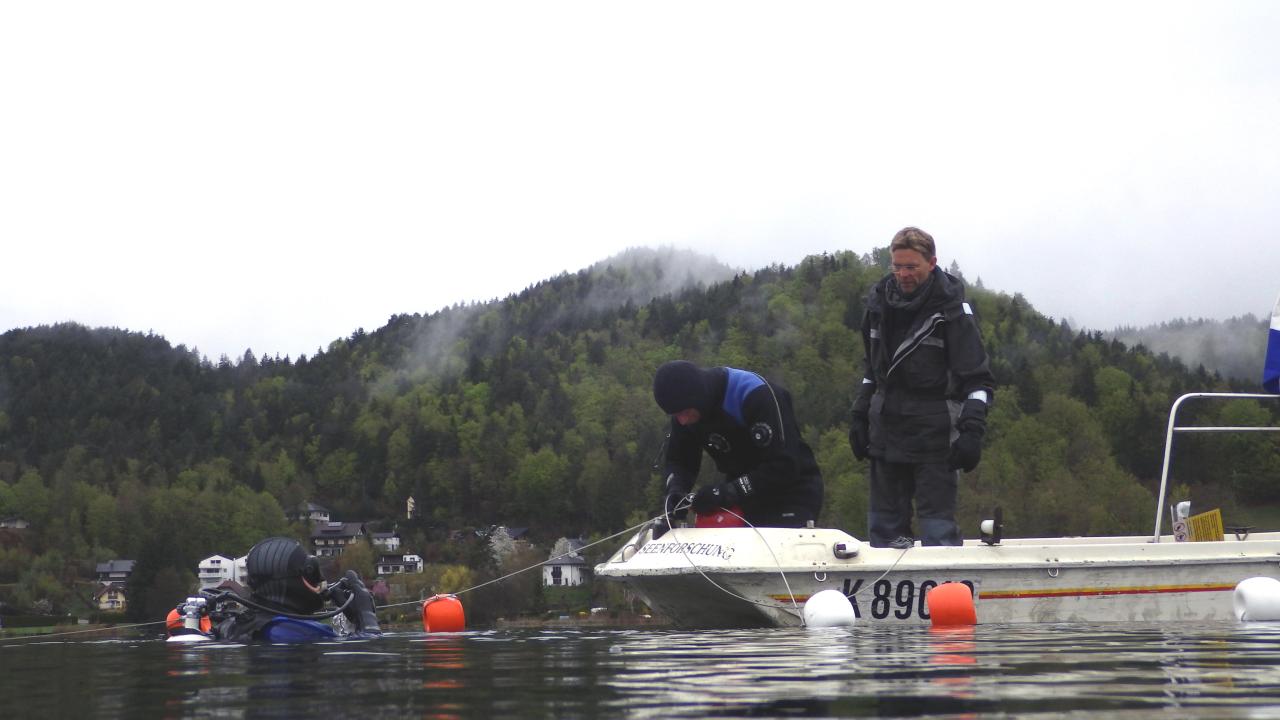 Vom Boot aus, werden die Bojen in den See eingebracht. Ein Taucher unterstütz dabei im Wasser