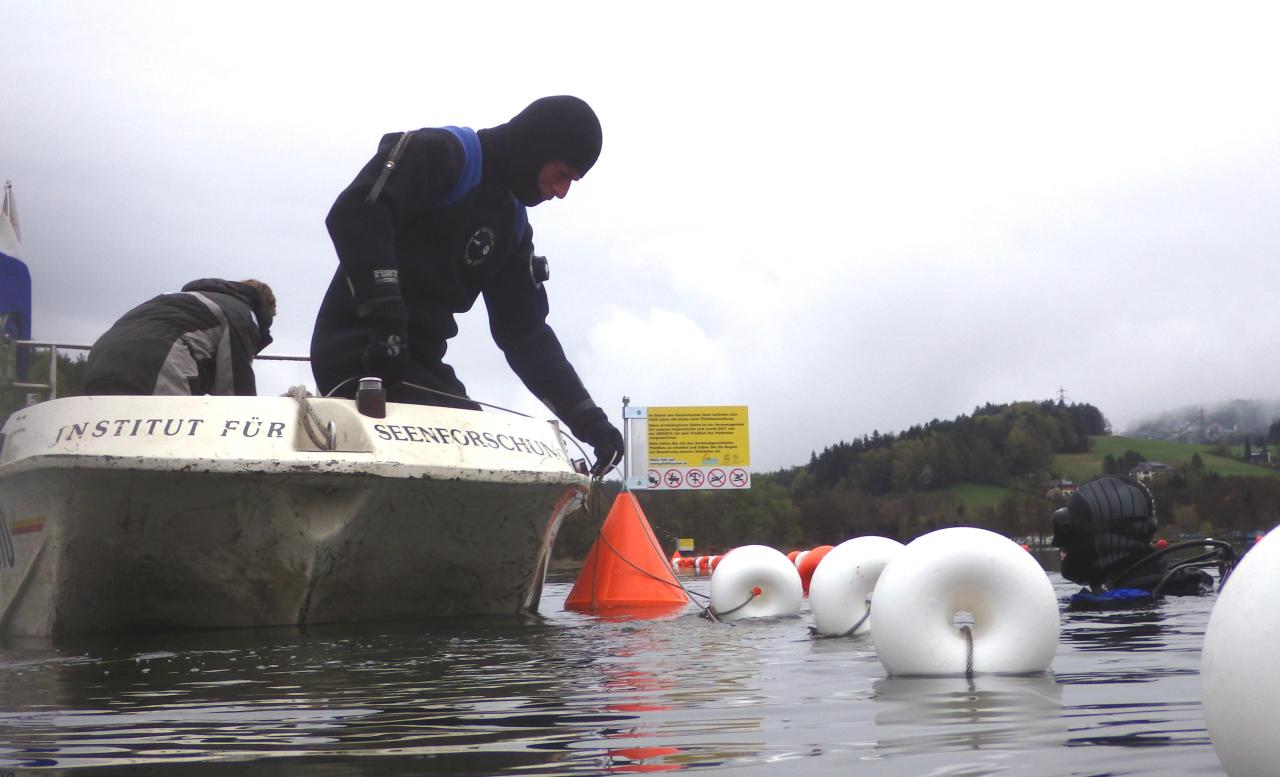 Ein Mann im Tauchanzug an Bord eines Bootes setzt Markierungsbojen in den See